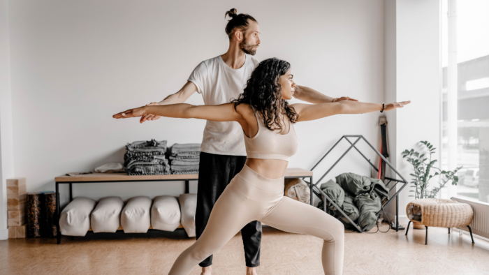 A white man assisting a woman of color in a yoga pose.