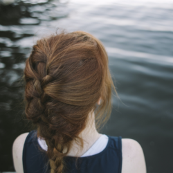 Picture of a white female with red hair in a French braid overlooking water.