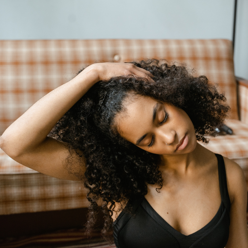 A Black woman wearing workout gear and stretching her neck with her hand on her head and her ear to her chest | 5 Ways Yoga Can Improve Your Mental Health | Holy Yoga